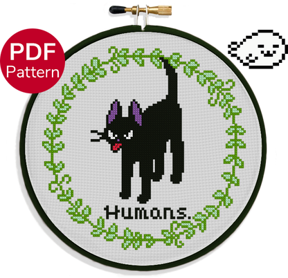 cross stitch pattern of a cat sticking his tongue out with an angry face with the text 'humans.' under it