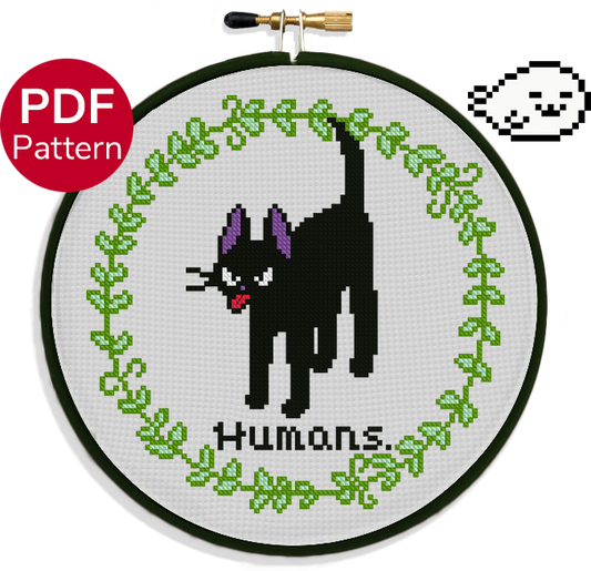 cross stitch pattern of a cat sticking his tongue out with an angry face with the text 'humans.' under it