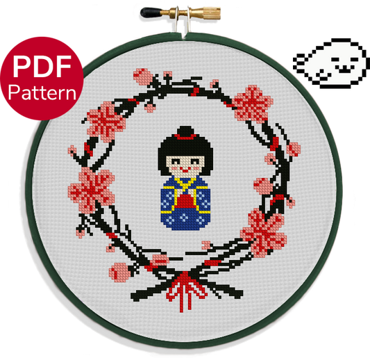 cross stitch pattern of a japanese wooden doll wearing a blue kimono surrounded by a wreath of sakura leaves